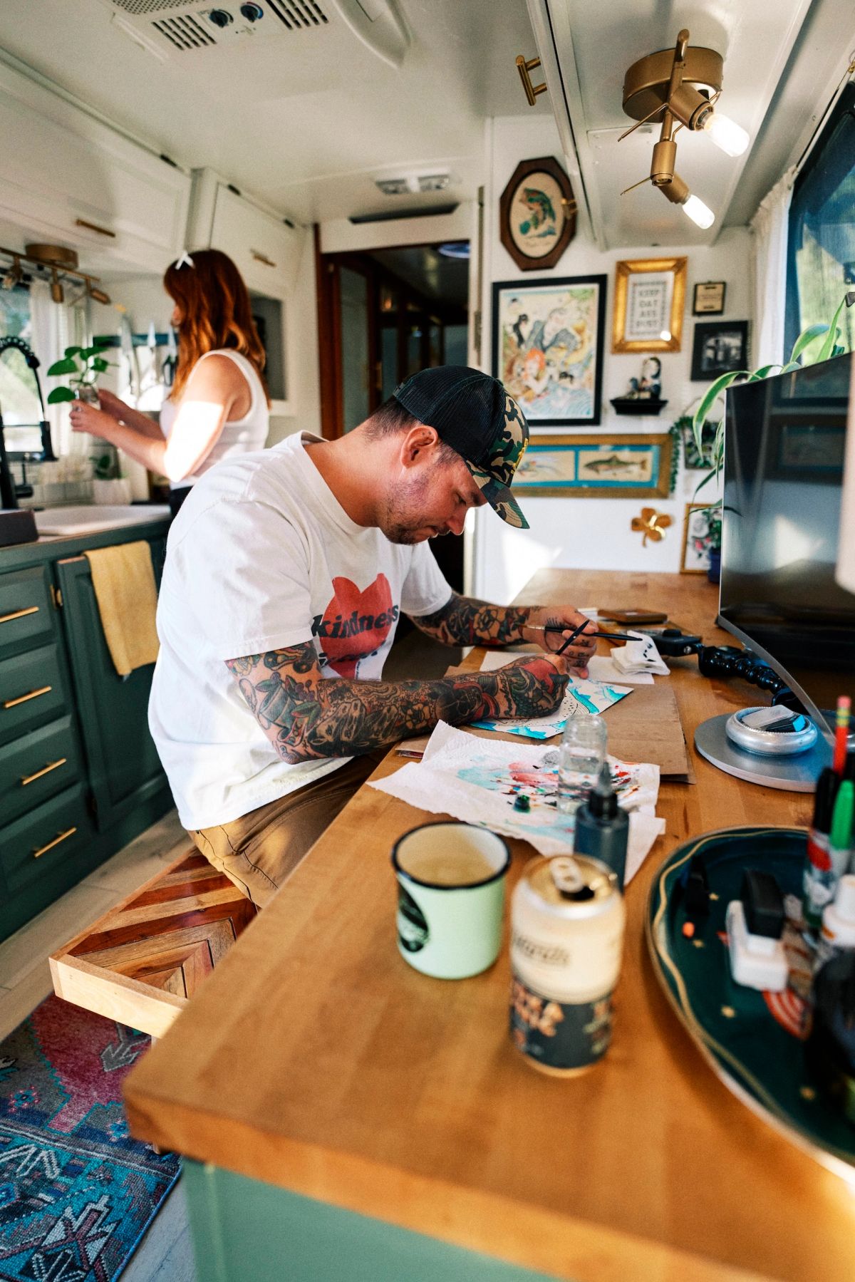 Inside of an airstream with Drew at work on a painting with a woman in the background